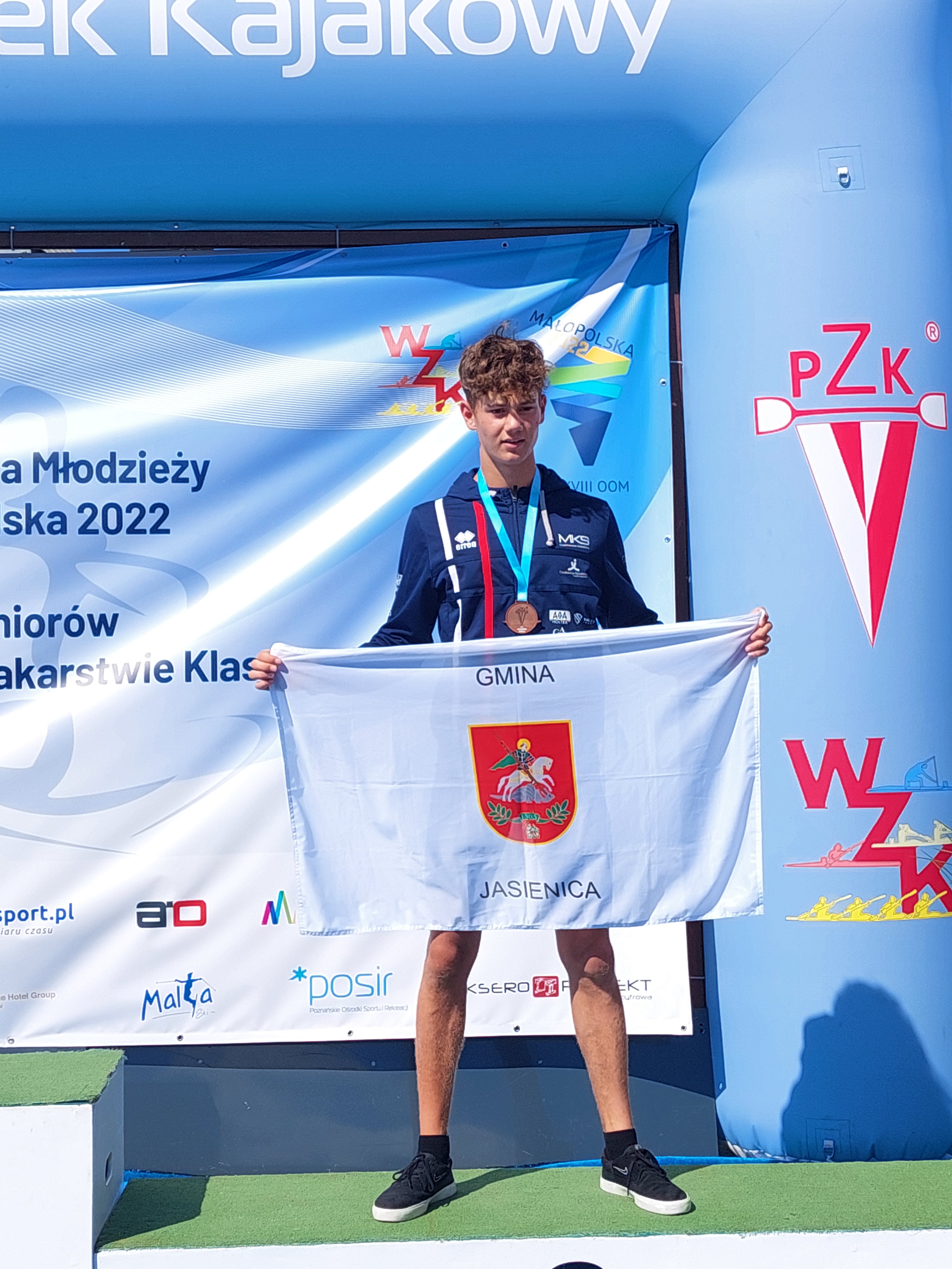 Bartosz Wizner na podium w rękach trzyma flagę gminy Jasienica.
