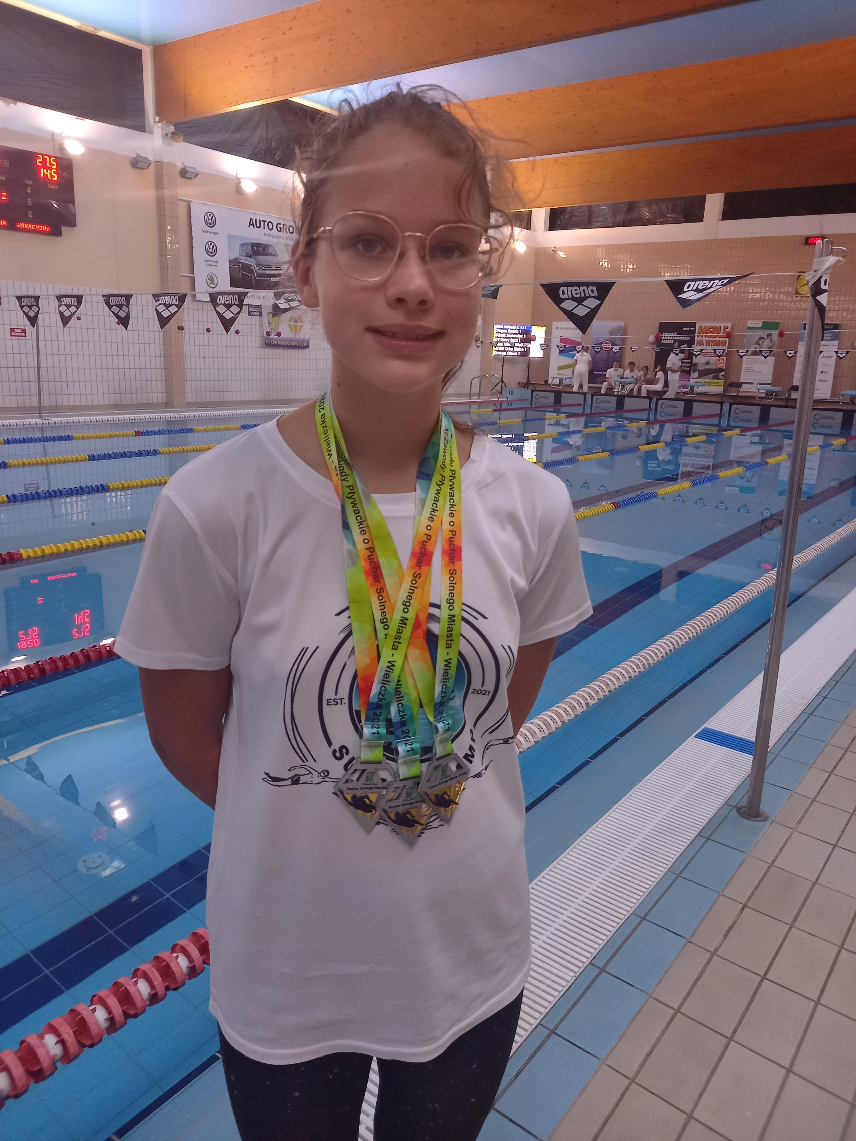 Karolina na pływalni pozuje z trzema medalami na szyi.